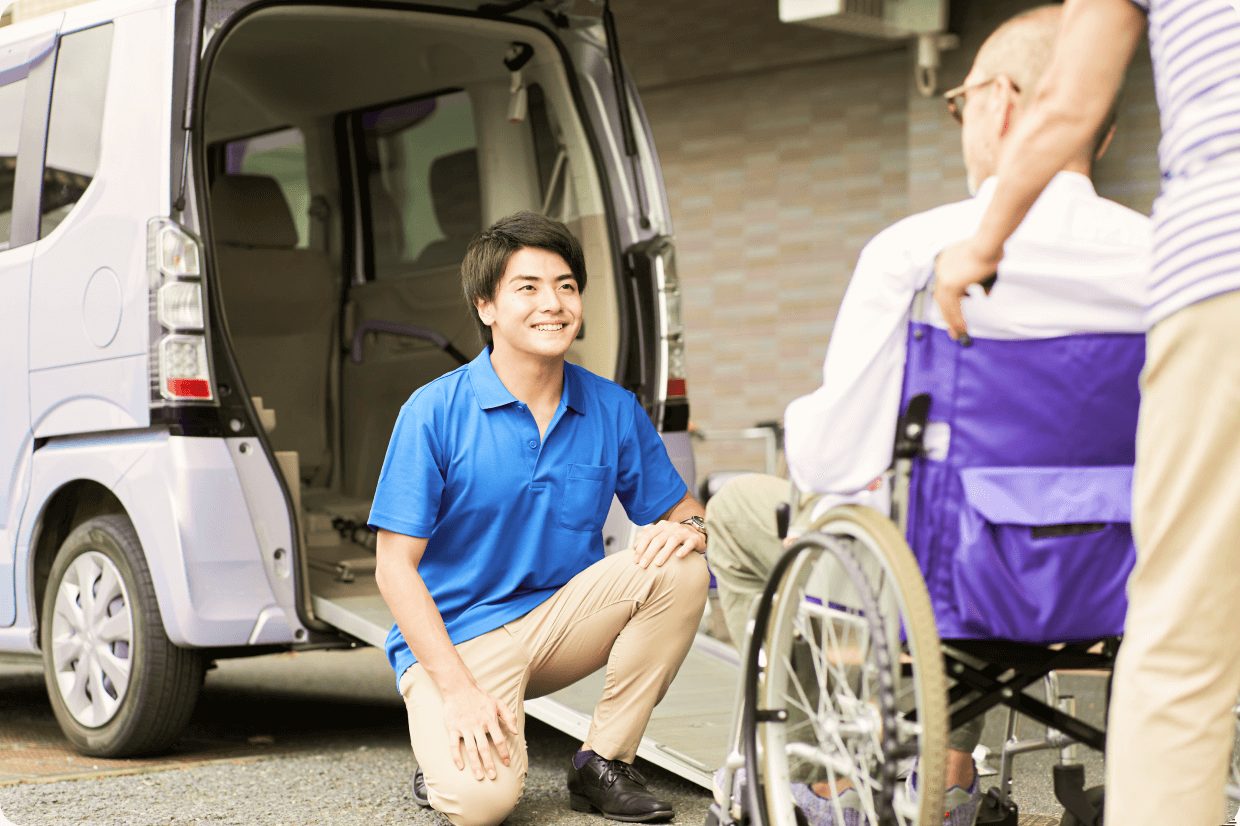 車いすに乗っている男性の介護タクシー利用者と、笑顔で車の前で迎える職員