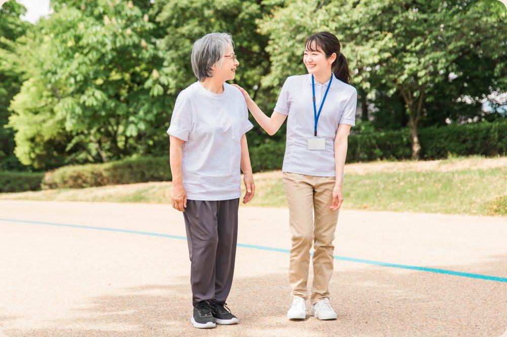 高齢女性と女性介護職員が談笑しながら屋外を散歩している様子